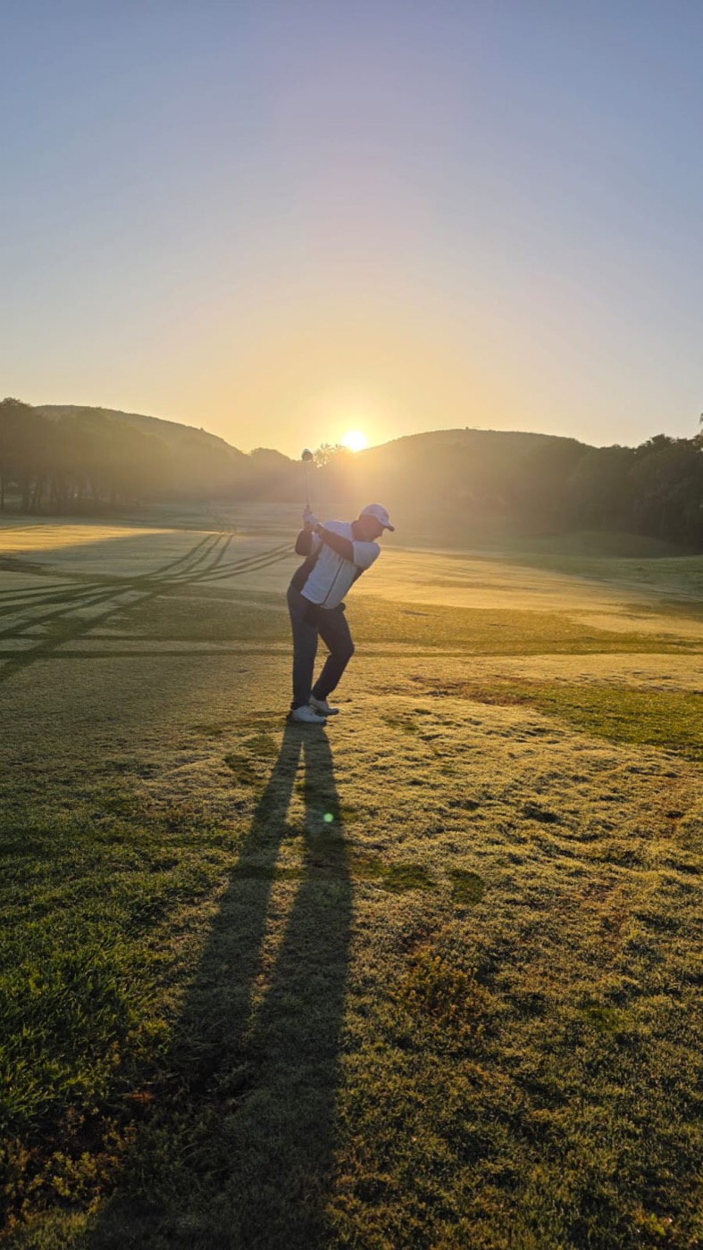 Domingo Loro en lo alto del backswing al amanecer, con su sombra larga sobre la calle del Real Club de Golf El Plantío.